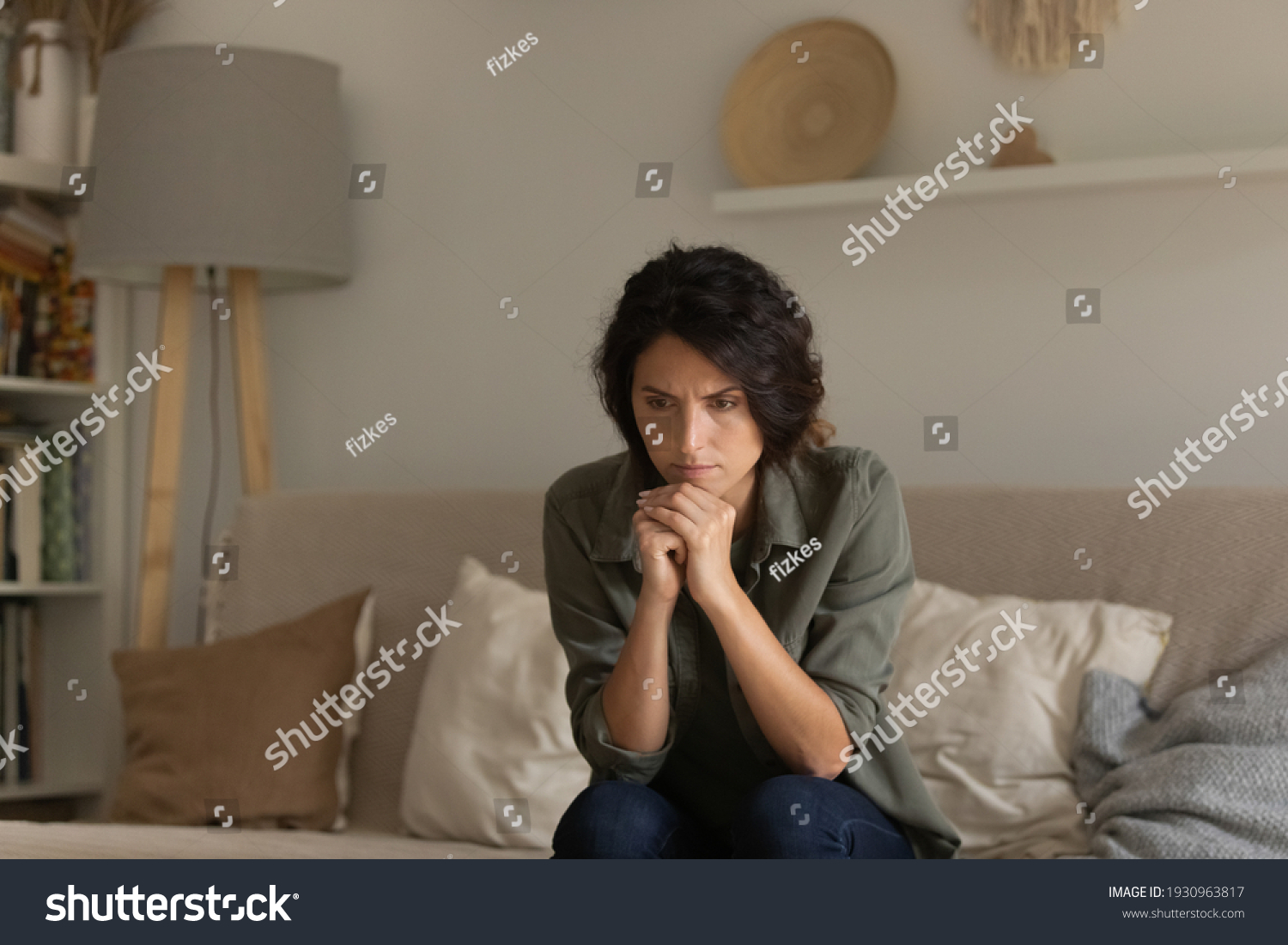 Critical situation. Thoughtful nervous young lady sit on sofa lean forward on folded hands try to keep emotions under control. Worried female think of overcoming bad life event ponder on hard decision #1930963817