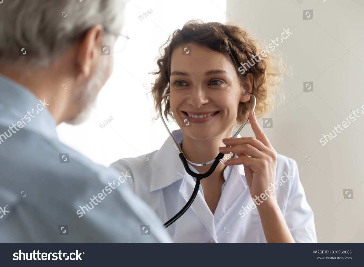 Close up of smiling young Caucasian female doctor use stethoscope examine mature patient heart rate in clinic. Happy caring woman nurse hold phonendoscope listen to elderly man heartbeat in hospital. #1930968068