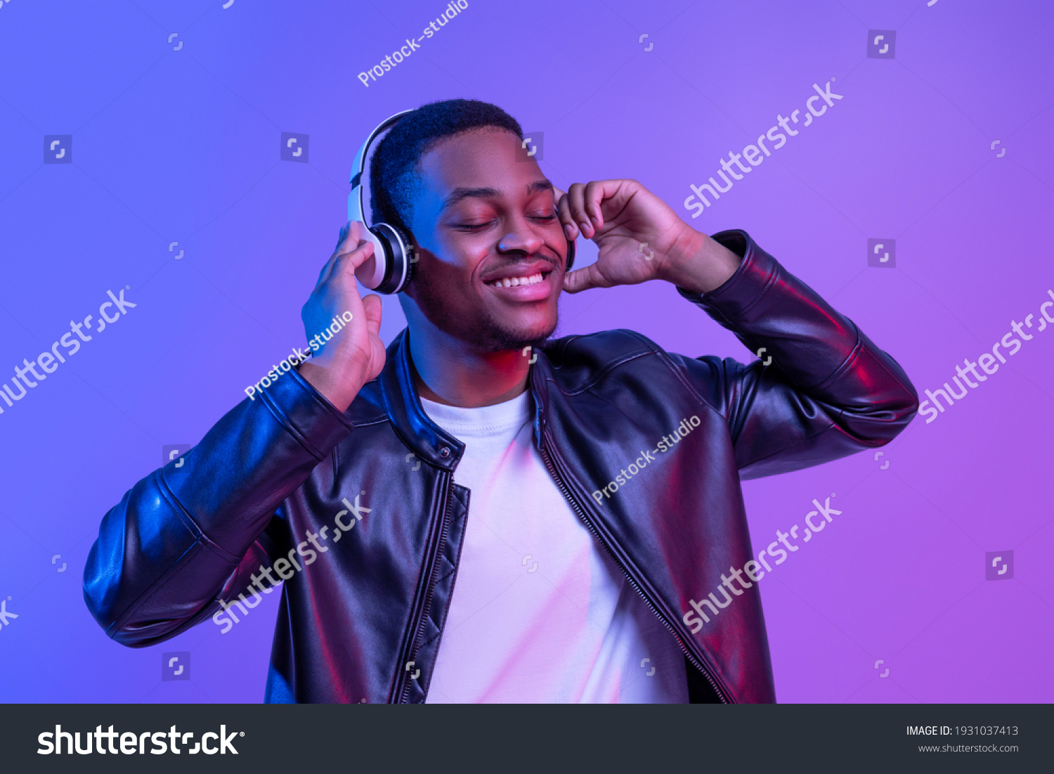 Music Lover. Handsome Black Guy In Wireless Headphones And Leather Jacket Listening His Favorite Songs, Relaxed African American Man Standing With Closed Eyes Under Neon Light Over Purple Background #1931037413