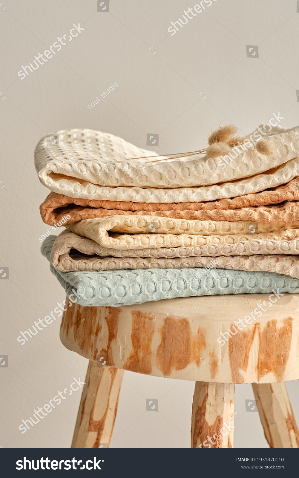 Collection of natural muslin towels lies on an unusual wooden stool. Natural, soft, airy and stylish home textiles. #1931470010