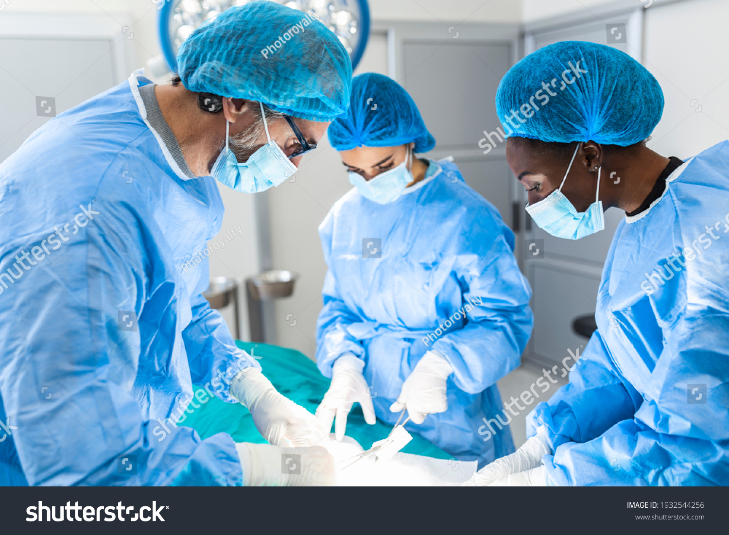 Group of surgeons doing surgery in hospital operating theater. Medical team doing critical operation. Group of surgeons in operating room with surgery equipment. Modern medical background #1932544256
