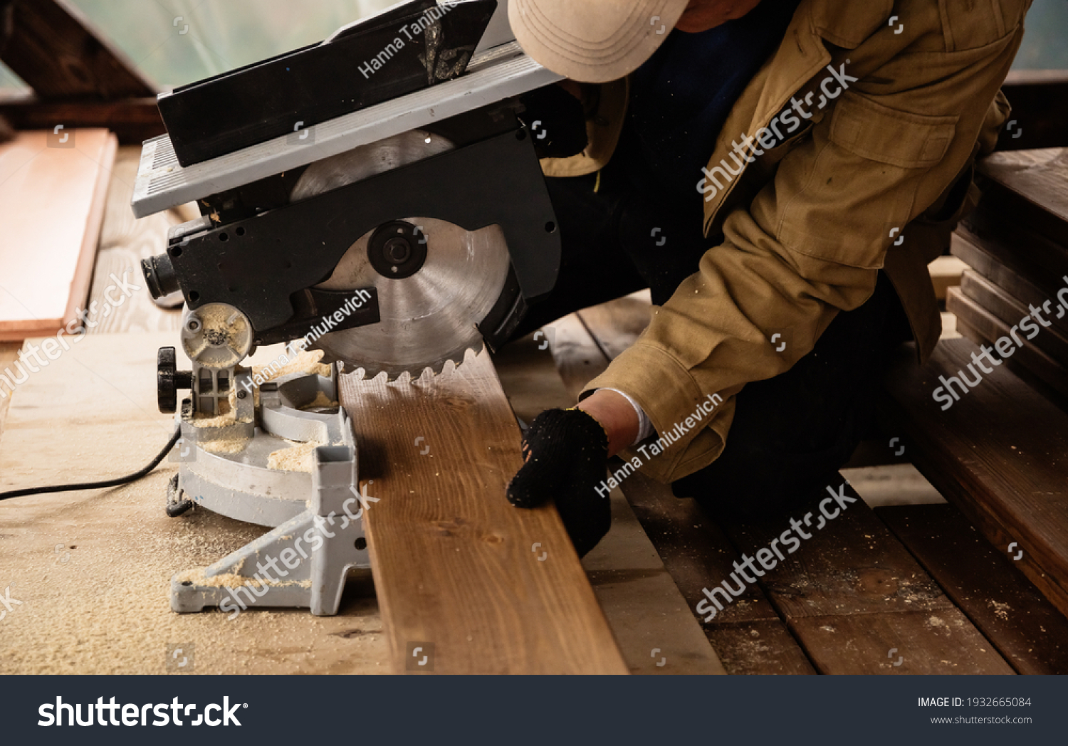 Miter saw with a large metal blade in the hands of a carpenter. Working tool for sawing wooden planks. A close-up of the sawing process. Labor protection and safety rules for the use of power tools. #1932665084