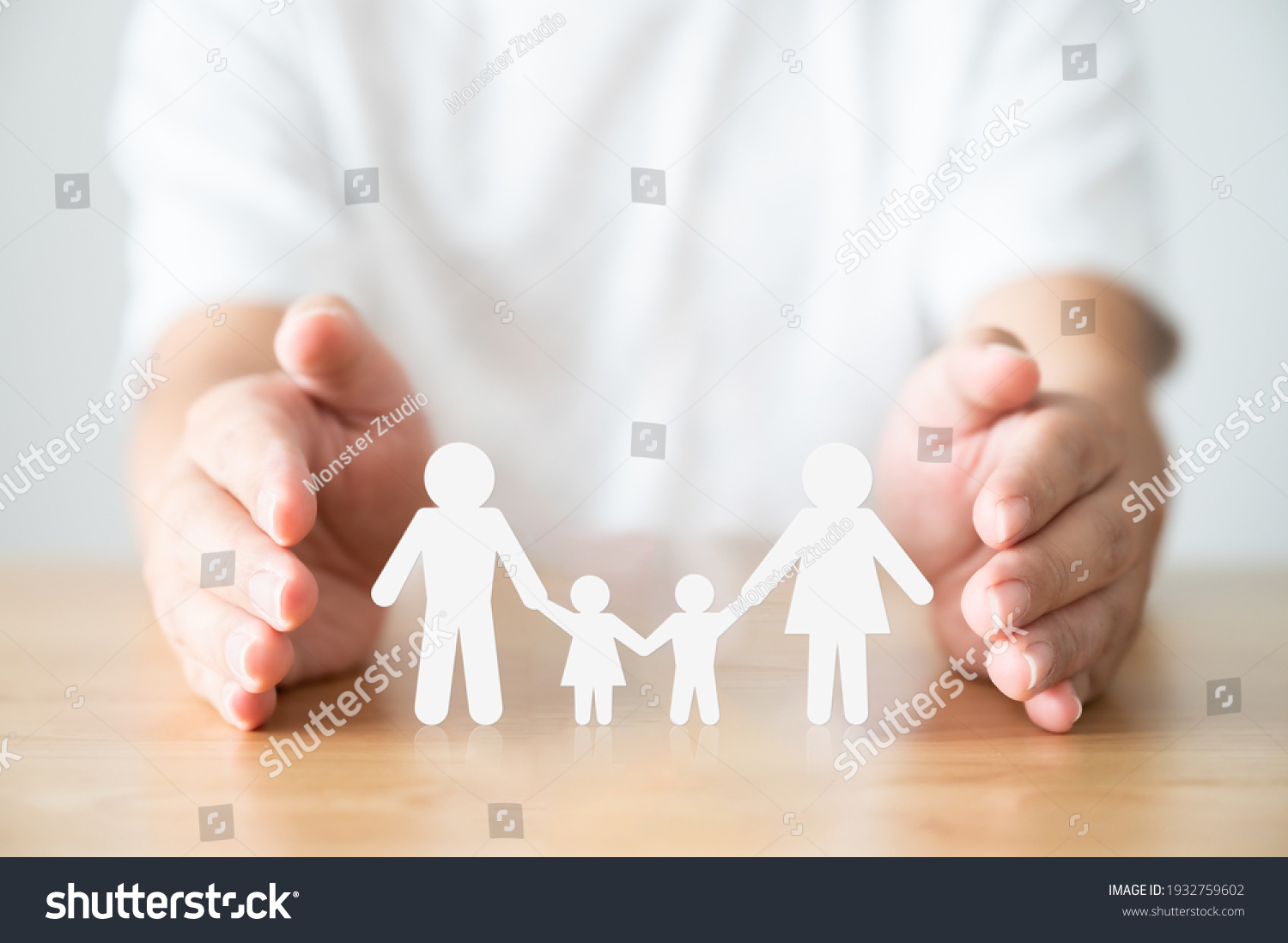 Hand protecting family on wood table. Healthcare and life insurance concept #1932759602