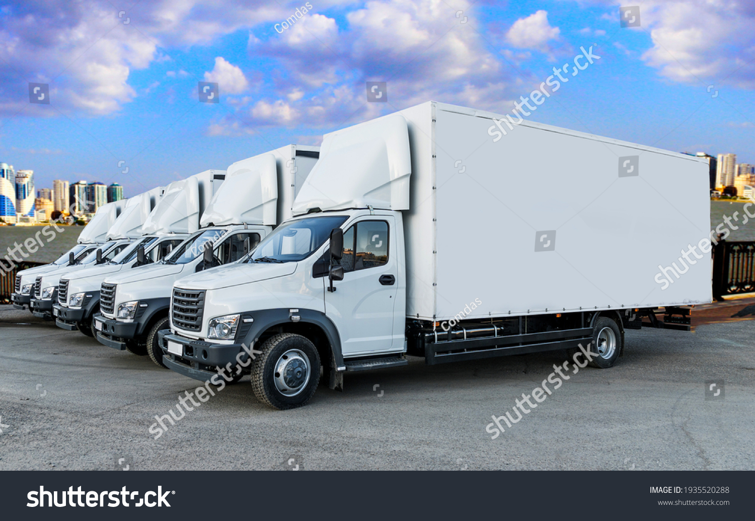 Some trucks are parked in a parking lot next to a logistics warehouse by the river. Several trucks are lined up in the parking lot. Logistic transport #1935520288