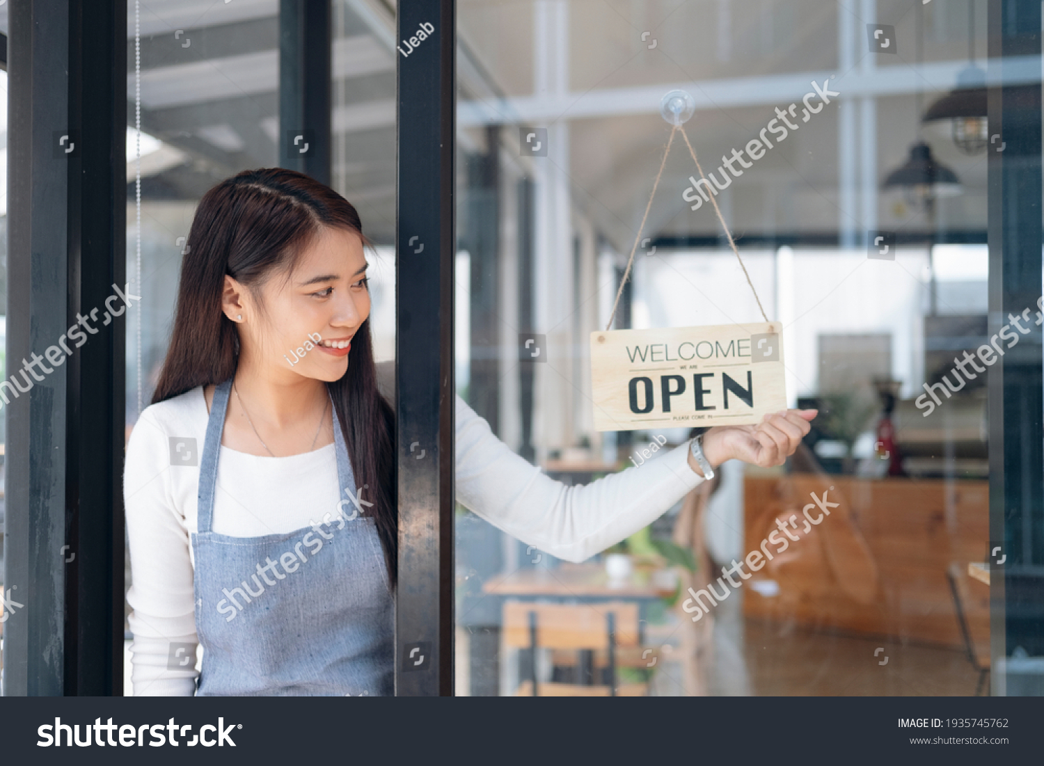 Small business owner smiling while turning the sign for the reopening of the place after the quarantine due to covid-19. Close up of woman hands holding sign now we are open support local business. #1935745762
