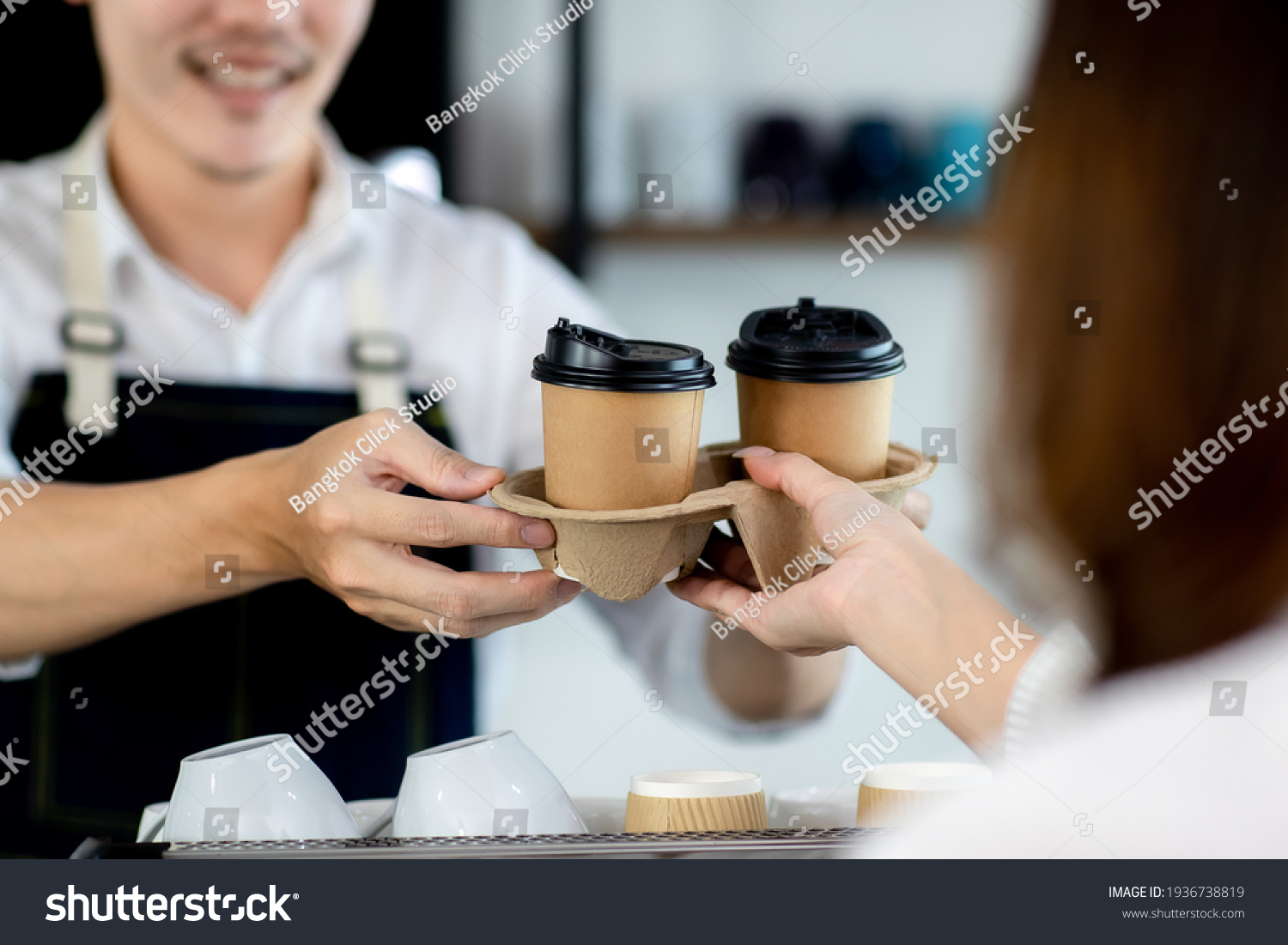 Close up hand. Asian young man or bartender serving paper coffee glass customer at coffee shop. making coffee in cafe. Concept sale paper bag and coffee. maker machine with portafilter #1936738819