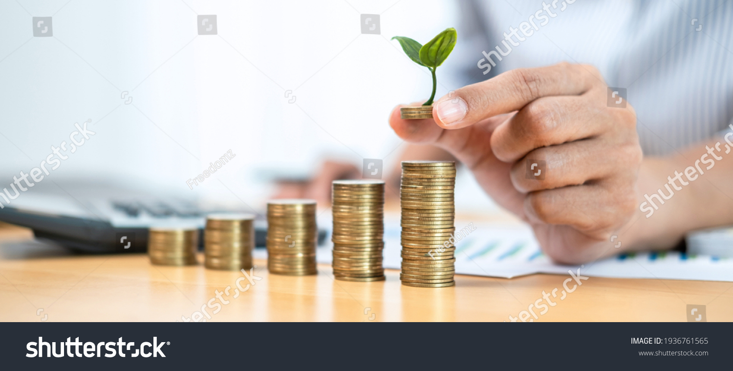 Close up of asian business woman holding coin with tree growing to putting on stacking coin about finance and accounting while the idea of increasing profit from business investment #1936761565