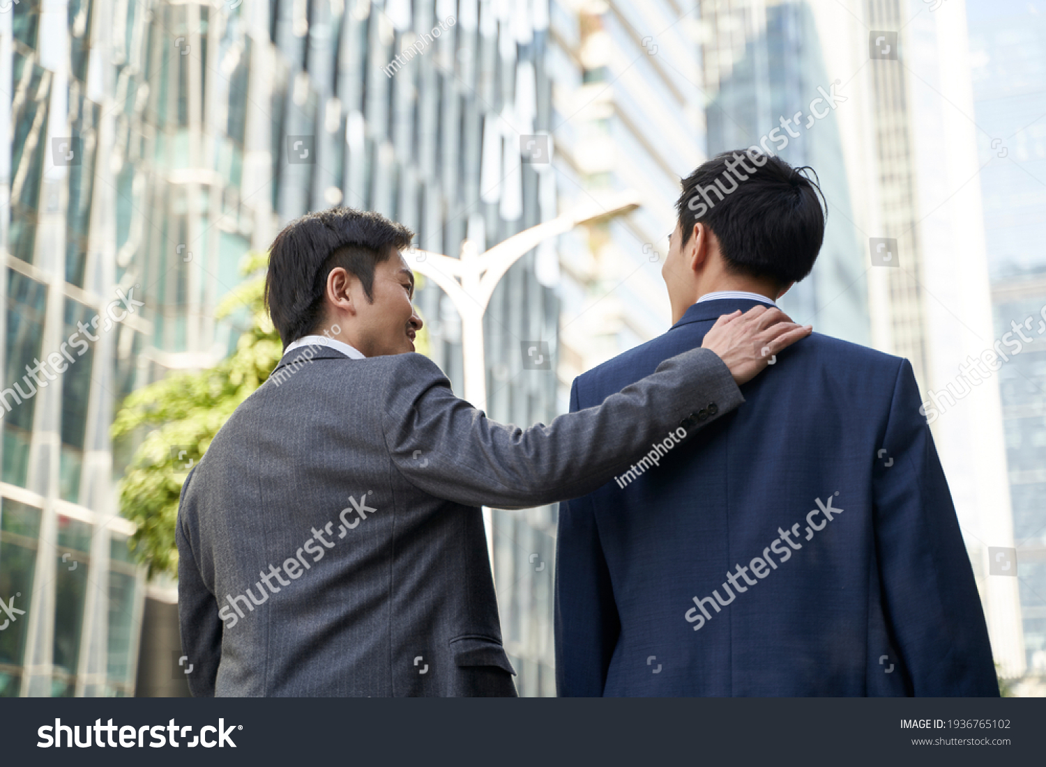 asian corporate executive giving subordinate a pat on the back while walking in street of central business district of modern city #1936765102