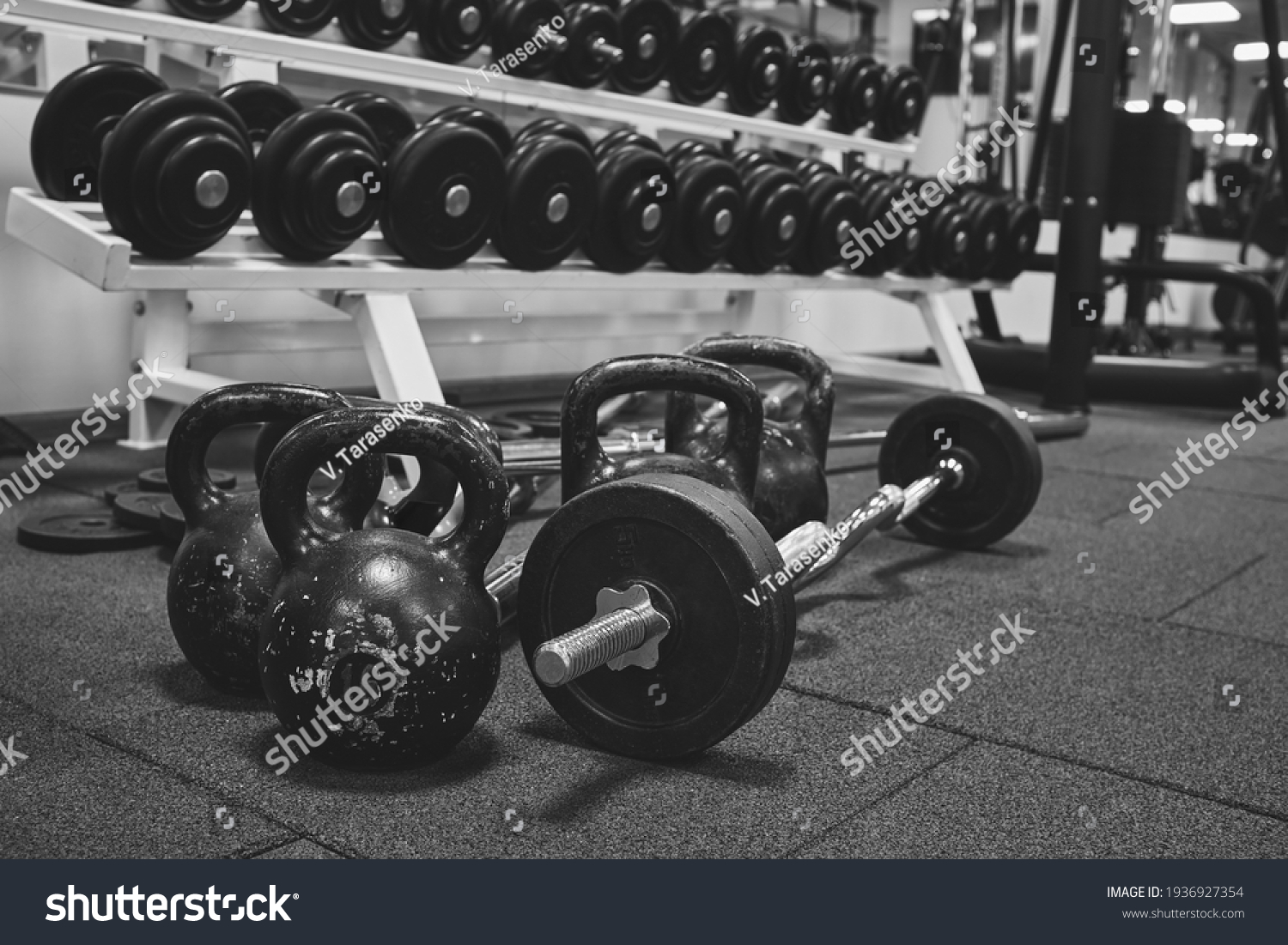 Dumbbells and kettlebells on a floor. Bodybuilding equipment. Fitness or bodybuilding concept background. black and white photography #1936927354