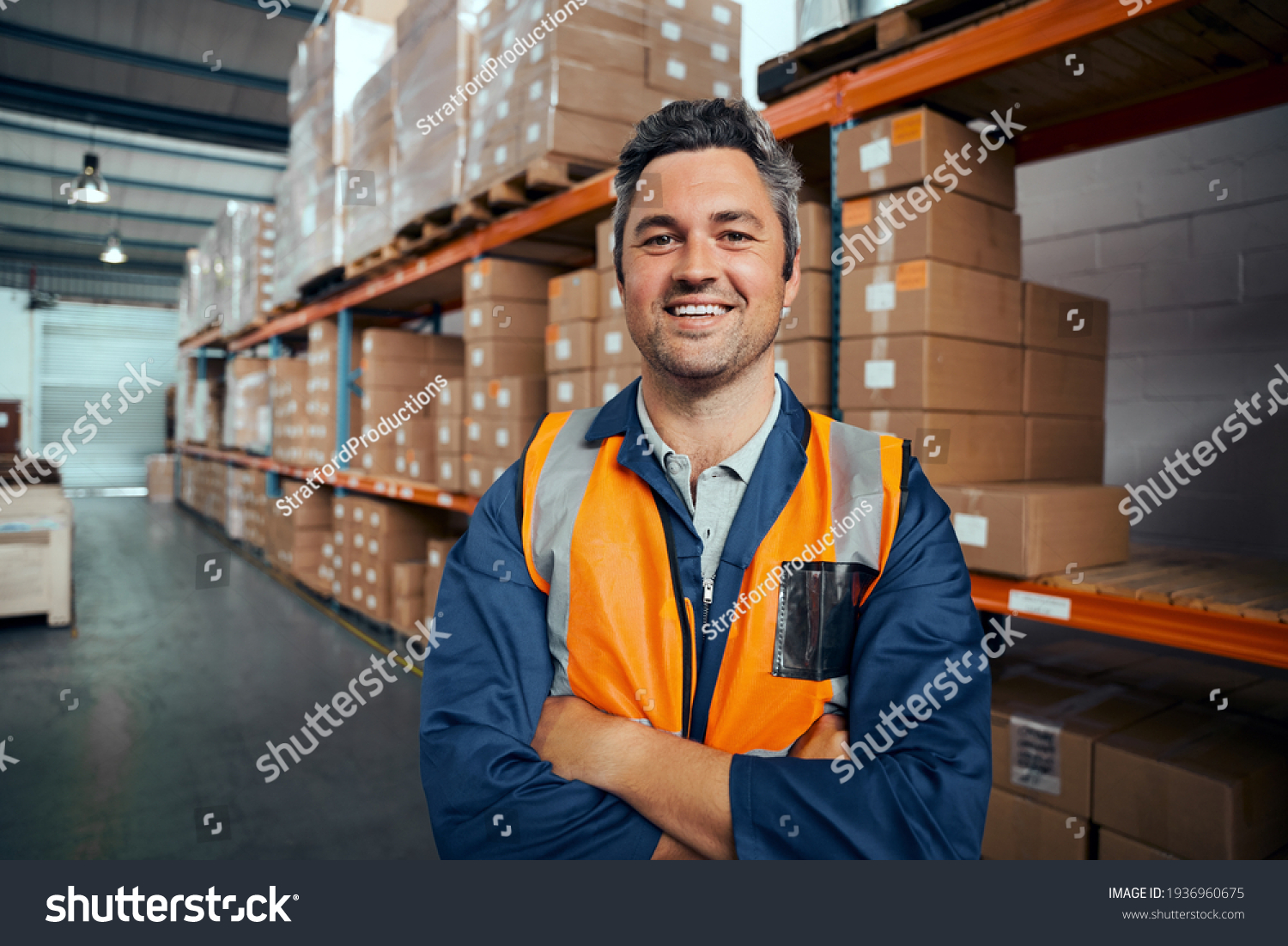 Smiling portrait of a male supervisor standing in warehouse with his arm crossed looking at camera #1936960675