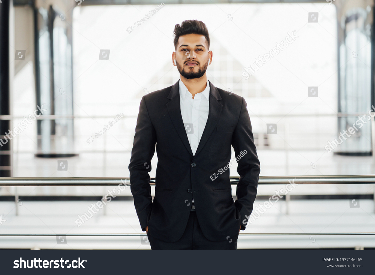 Bearded Indian man in a black suit in the middle of a modern building, office space, Indian businessman, bank employee. #1937146465