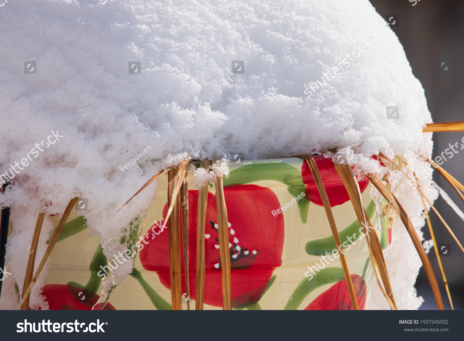 Snow covered flower pot with snow build up around it.  Drifted snow on top of large floral flower pot.   #1937345932