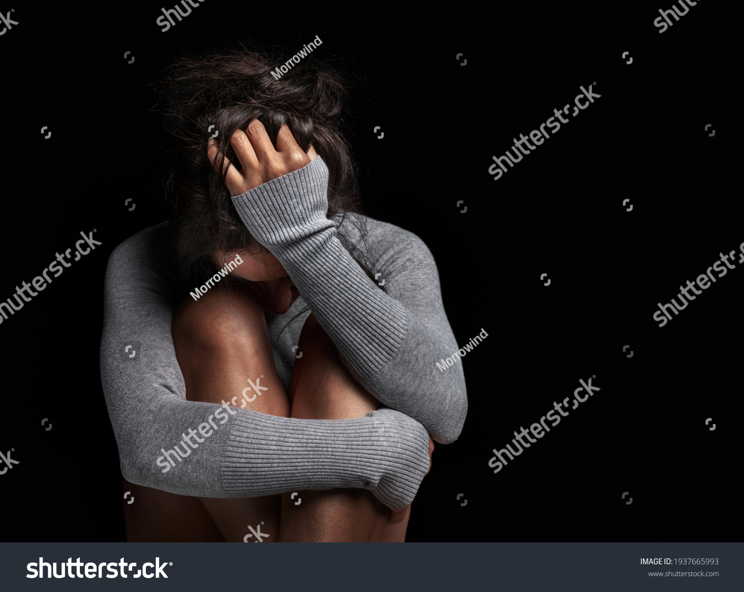 Depression or domestic violence concept: Sad lonely young woman crying while sitting in dark room with an attitude of sadness and boredom with her legs together and hugged. #1937665993