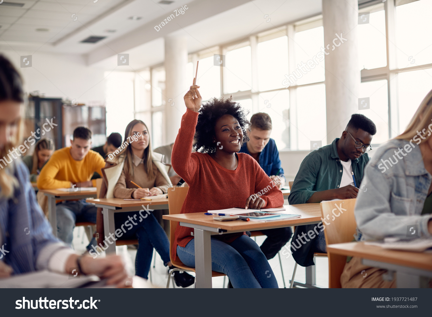 Happy African American student raising her hand to ask a question during lecture in the classroom.  #1937721487