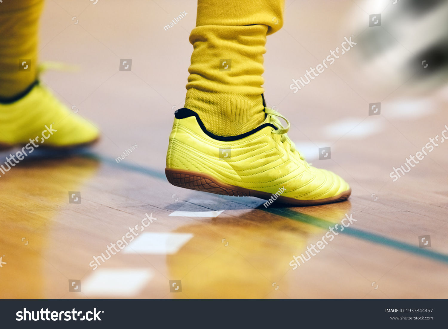 Indoor football player and classic ball. Futsal training for children. Legs of young futsal player in soccer cleats and socks. Indoor sports hall. Player in uniform. Junior level sport background #1937844457