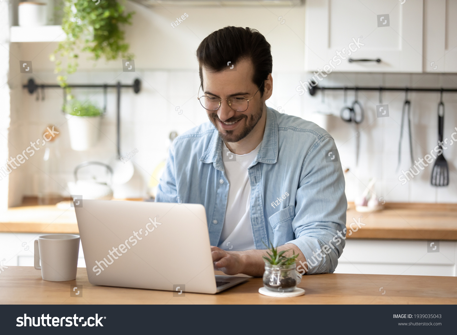 Smiling young guy in glasses enjoying online communication, typing message in social networks on computer. Happy millennial male client involved in using software application, people and technology. #1939035043