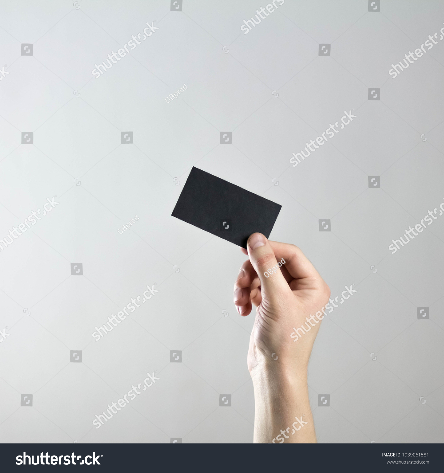 The hand holds an empty black business card. A clean flyer in your hands. For your text. Isolated on a gray background. #1939061581