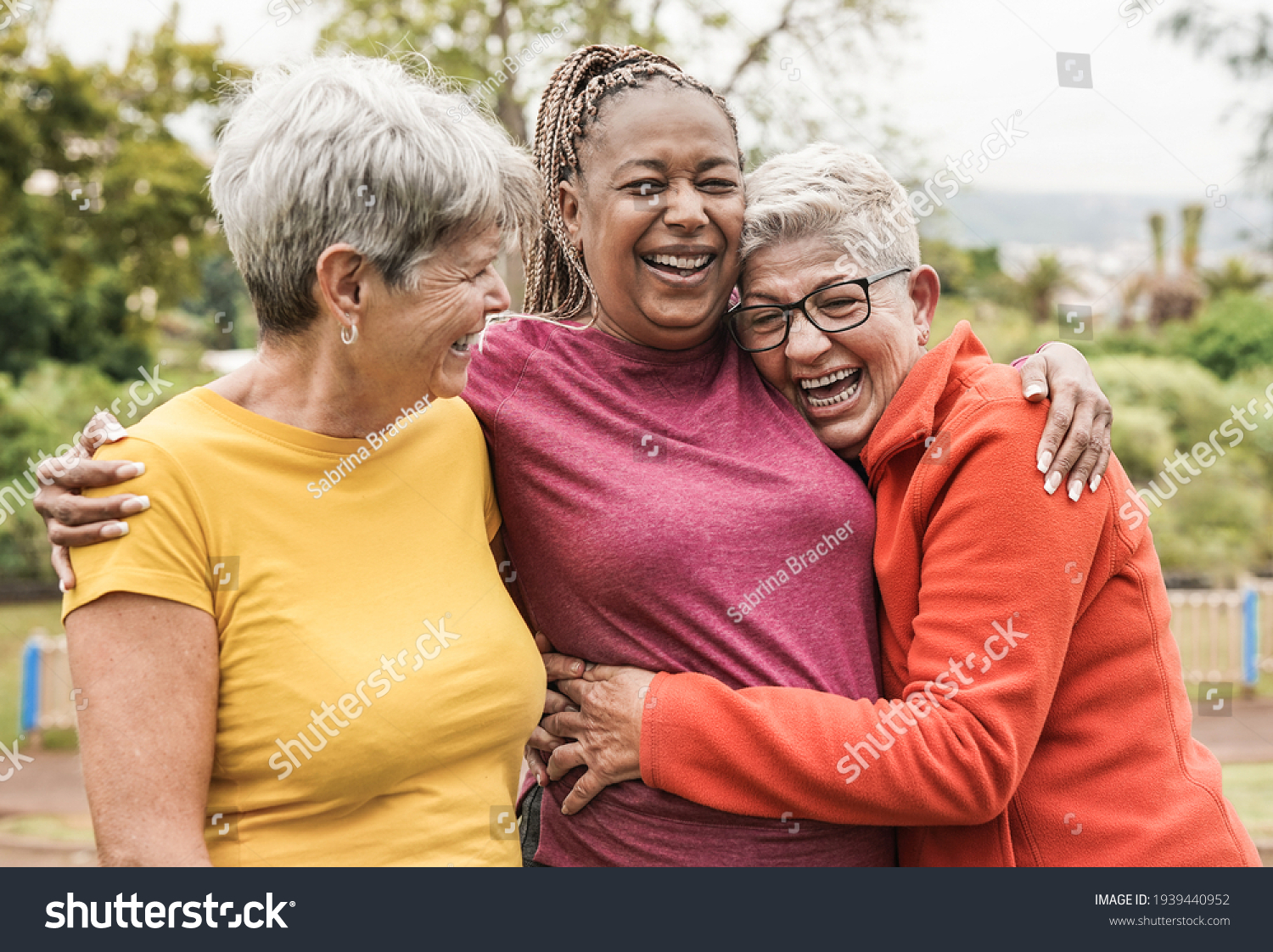 Happy multiracial senior women having fun together outdoor - Elderly generation people hugging each other at park #1939440952