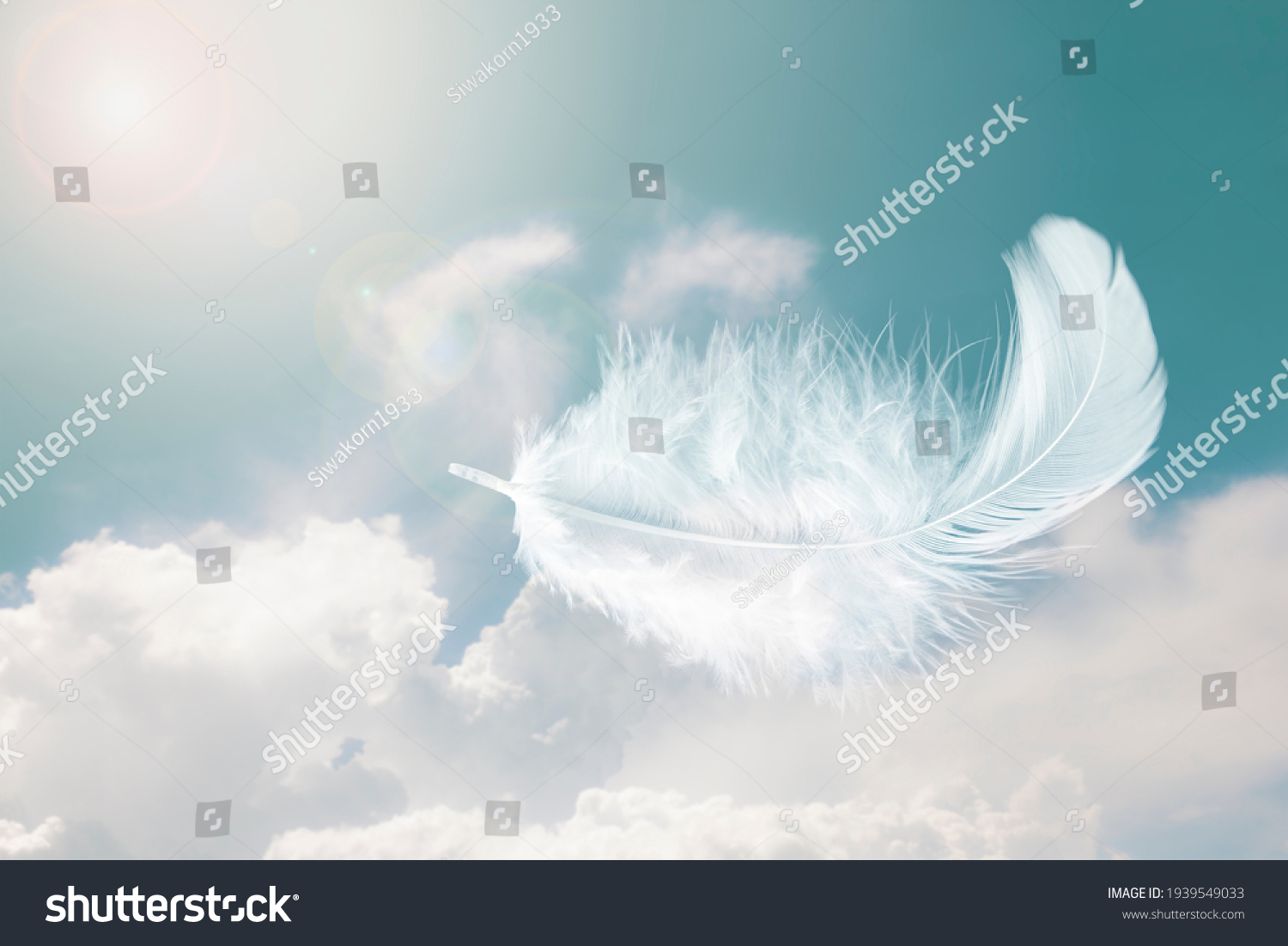 Beautiful Soft and Light White Fluffy Feathers Floating inThe Sky with Clouds. Abstract. Heavenly Dreamy Fluffy Colorful Sky. Swan Feather #1939549033