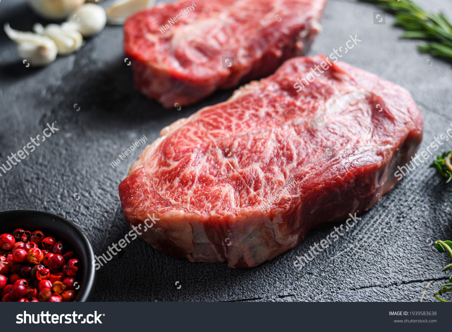 Raw top blade flat Ironcut, on black slate , bio marbled beef with herbs tomatoes peppercorns over grey stone surface background side close up . #1939583638