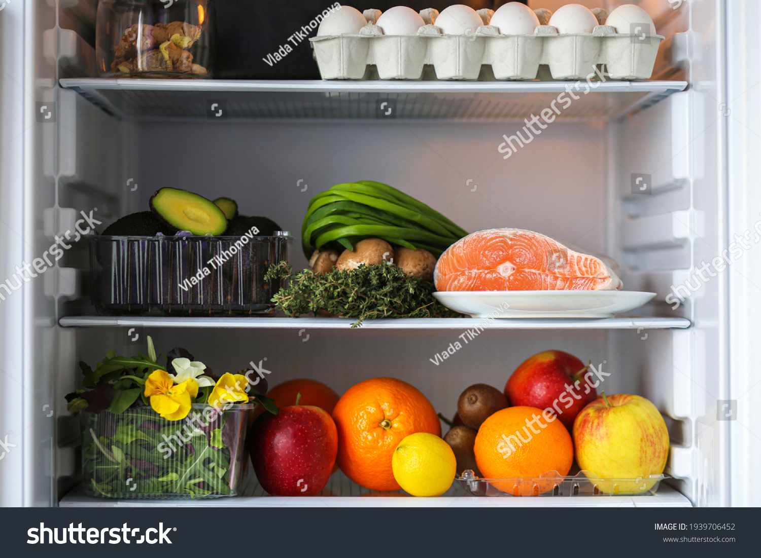 Open fridge with healthy food.Products on the shelves.Proper nutrition with red fish, avocado and fruits.Refrigerator with healthy products.Fruits, eggs, fish, avocado, mushrooms, herbs, kiwi, orange. #1939706452