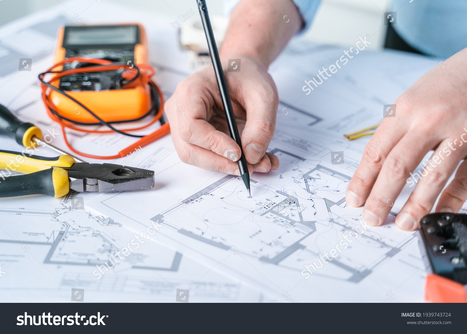 Man repairer making electricity project in house.Repairs planning.Drawing,diagrams,plan of electrification of apartment,building.Devices,accessories,voltmeter,wires,screwdriver,pliers and tape measure #1939743724