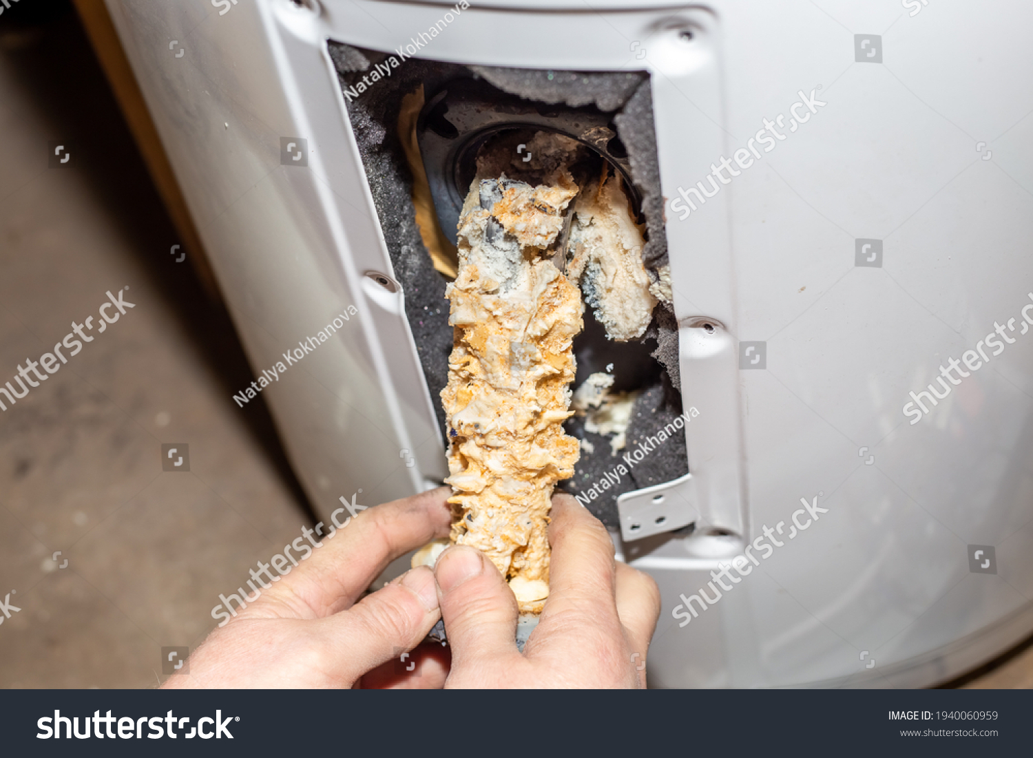 Repair and maintenance of boilers. The master plumber pulls out a tubular electric heater covered with lime scale from the hole in the boiler. #1940060959