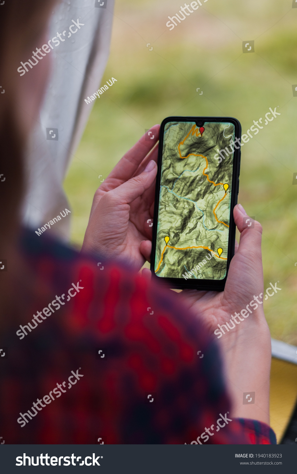 Women hands holding smartphone with app navigation hiking map on screen.  Mountains map with route and markers. Girl planning a trip inside the tent at the camp.  #1940183923