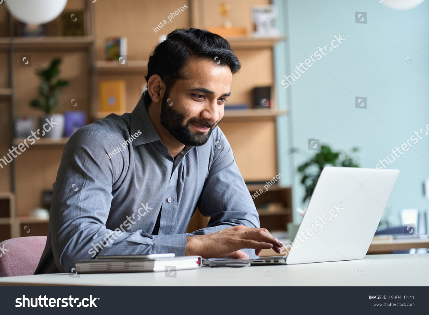 Smiling indian business man working on laptop at home office. Young indian student or remote teacher using computer remote studying, virtual training, watching online education webinar at home office. #1940410141