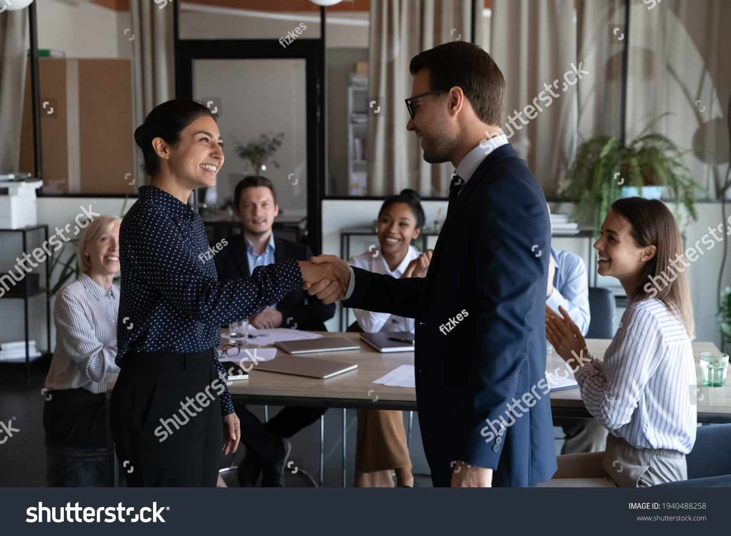 Smiling diverse multiracial employees handshake close deal agreement at meeting. Happy multiethnic businesspeople shake hand get acquainted greet at briefing, congratulate colleague with promotion. #1940488258
