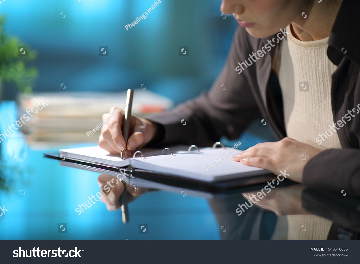 Close up of a woman hands taking notes in a ring binder notebook on a desk in the night at home #1940516635
