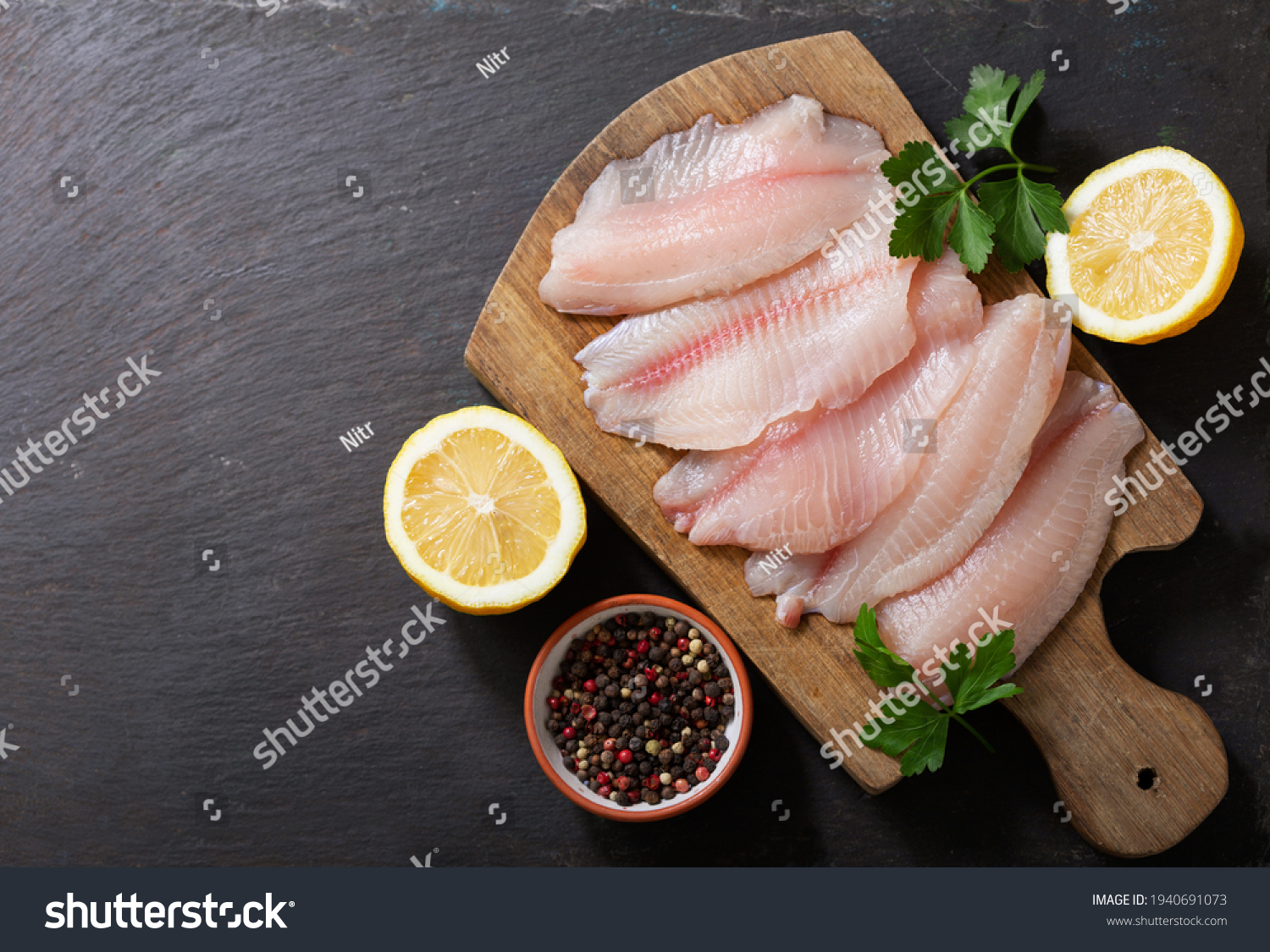 fresh fish fillet of tilapia with ingredients for cooking on wooden board, top view #1940691073