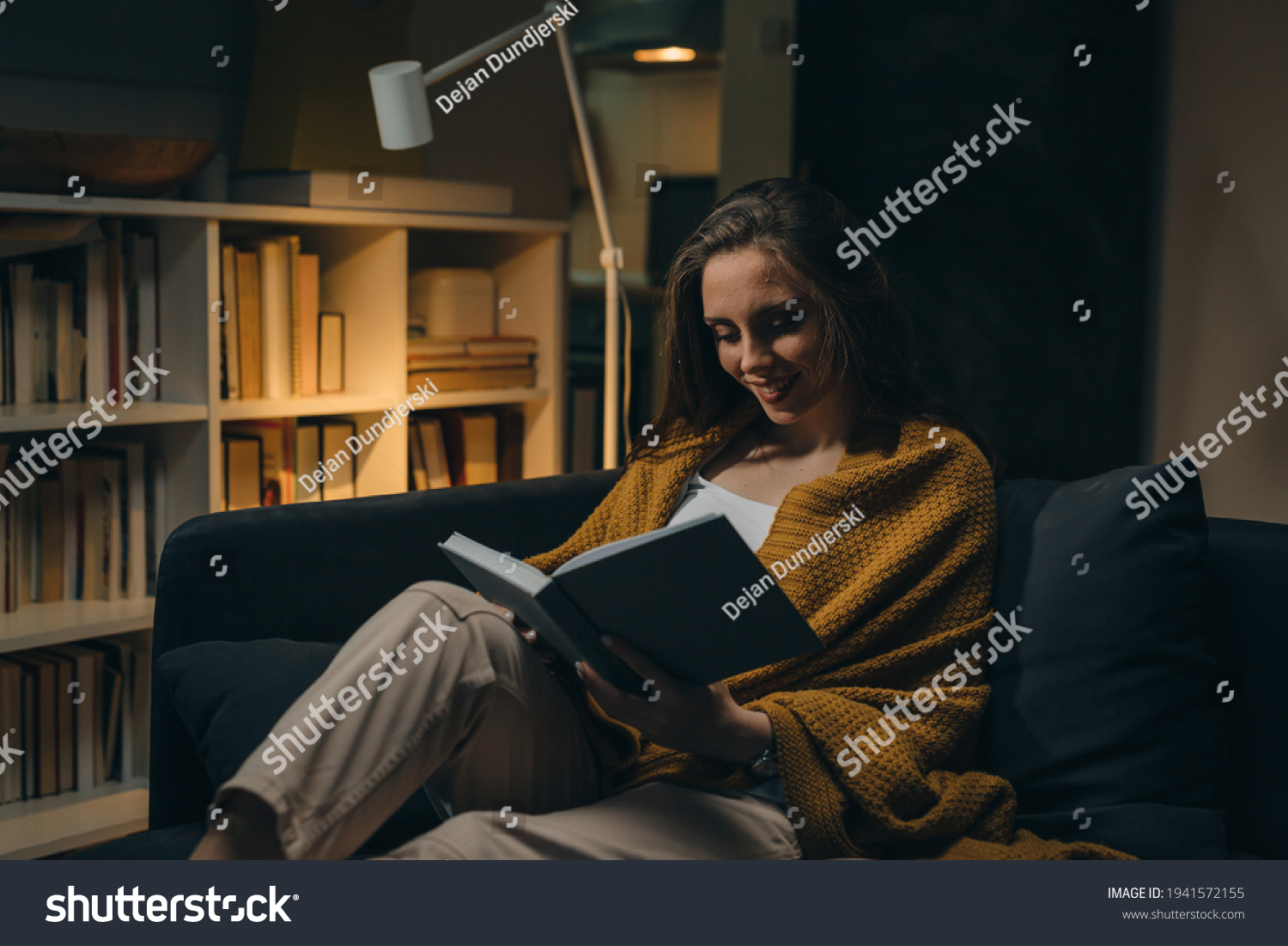 woman relaxing on sofa and reading book. evening moody ambience. she is enjoying time during weekend #1941572155