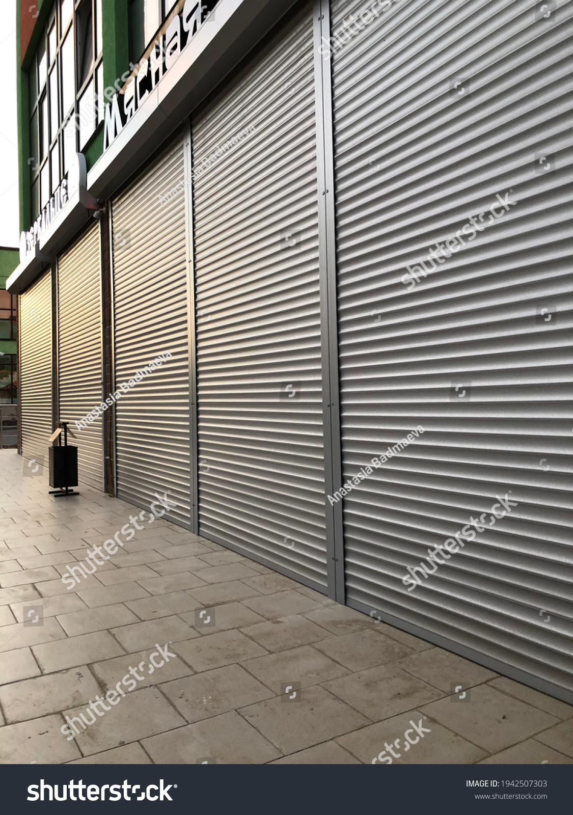Grey roller shutters of a small storewith some sun lights on it in a town. #1942507303