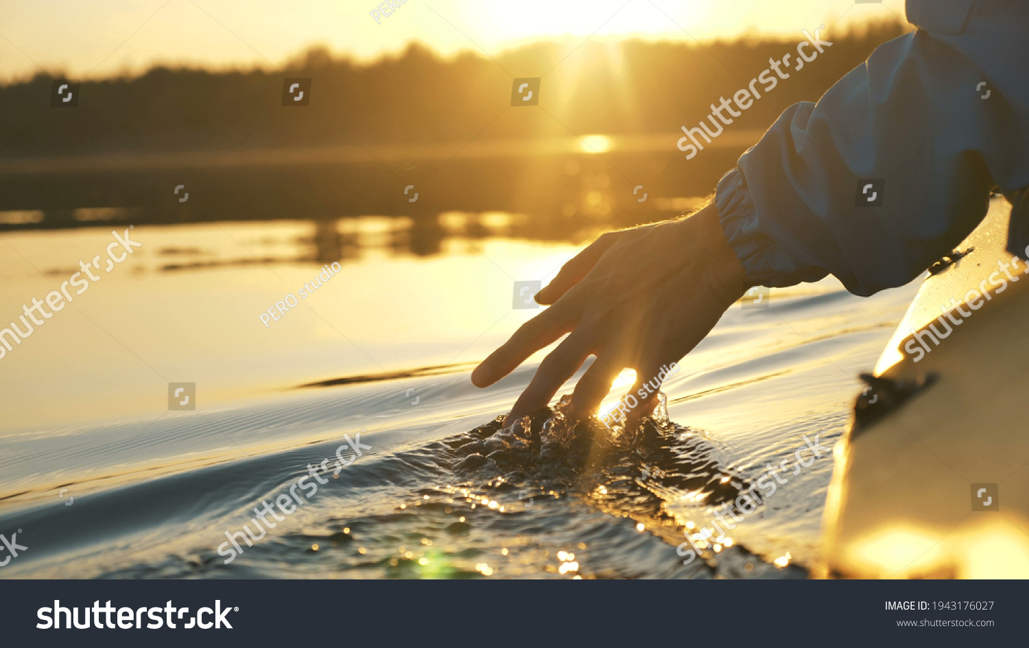 man puts fingers down in lake kayaking against backdrop of golden sunset, unity harmony nature #1943176027