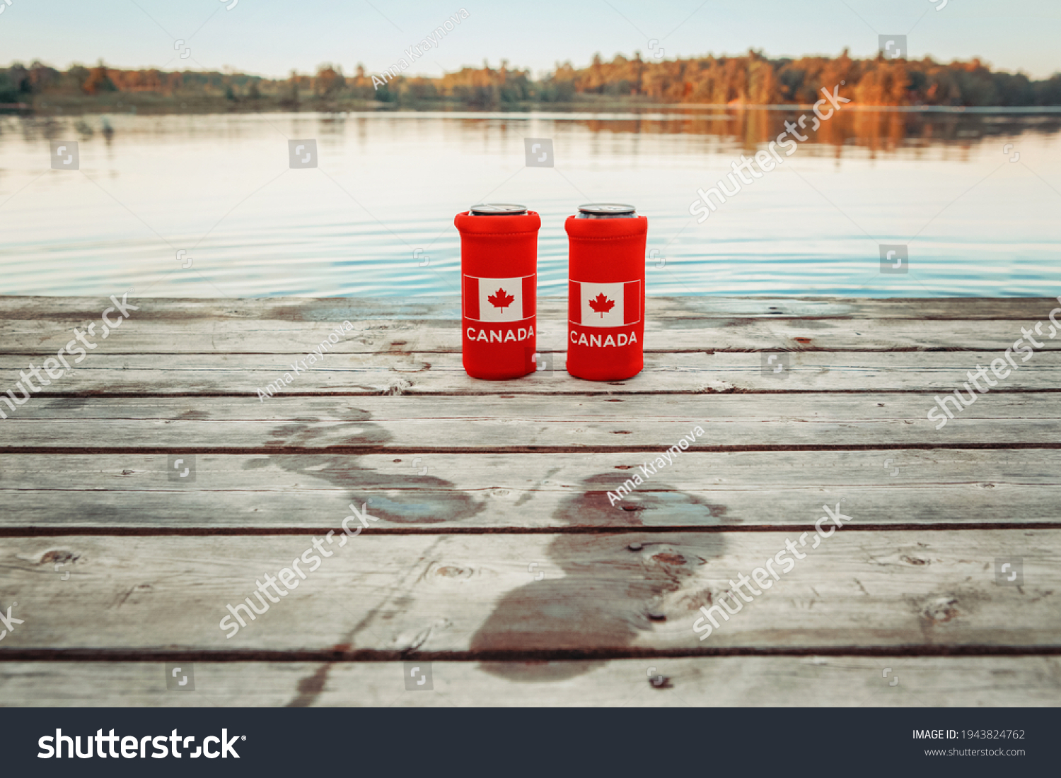 Two cans of beer in red cozy beer can coolers with Canadian flag standing on wooden pier by lake outdoors. Wet footprints on wooden dock. Friends celebrating Canada Day national celebration by water.  #1943824762