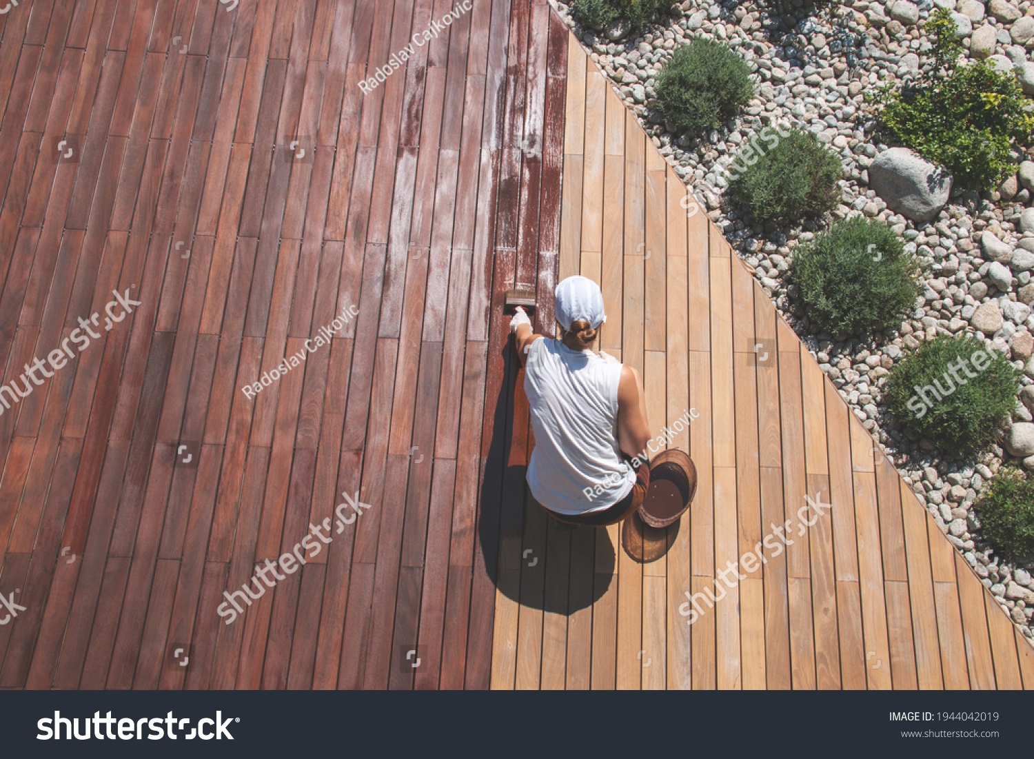 Wood deck renovation treatment, the person applying protective wood stain with a brush, overhead view of ipe hardwood decking restoration process #1944042019