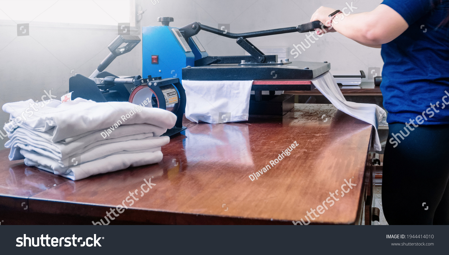 woman manipulating a sublimation machine ironing a shirt. advertising and screen printing concept. #1944414010