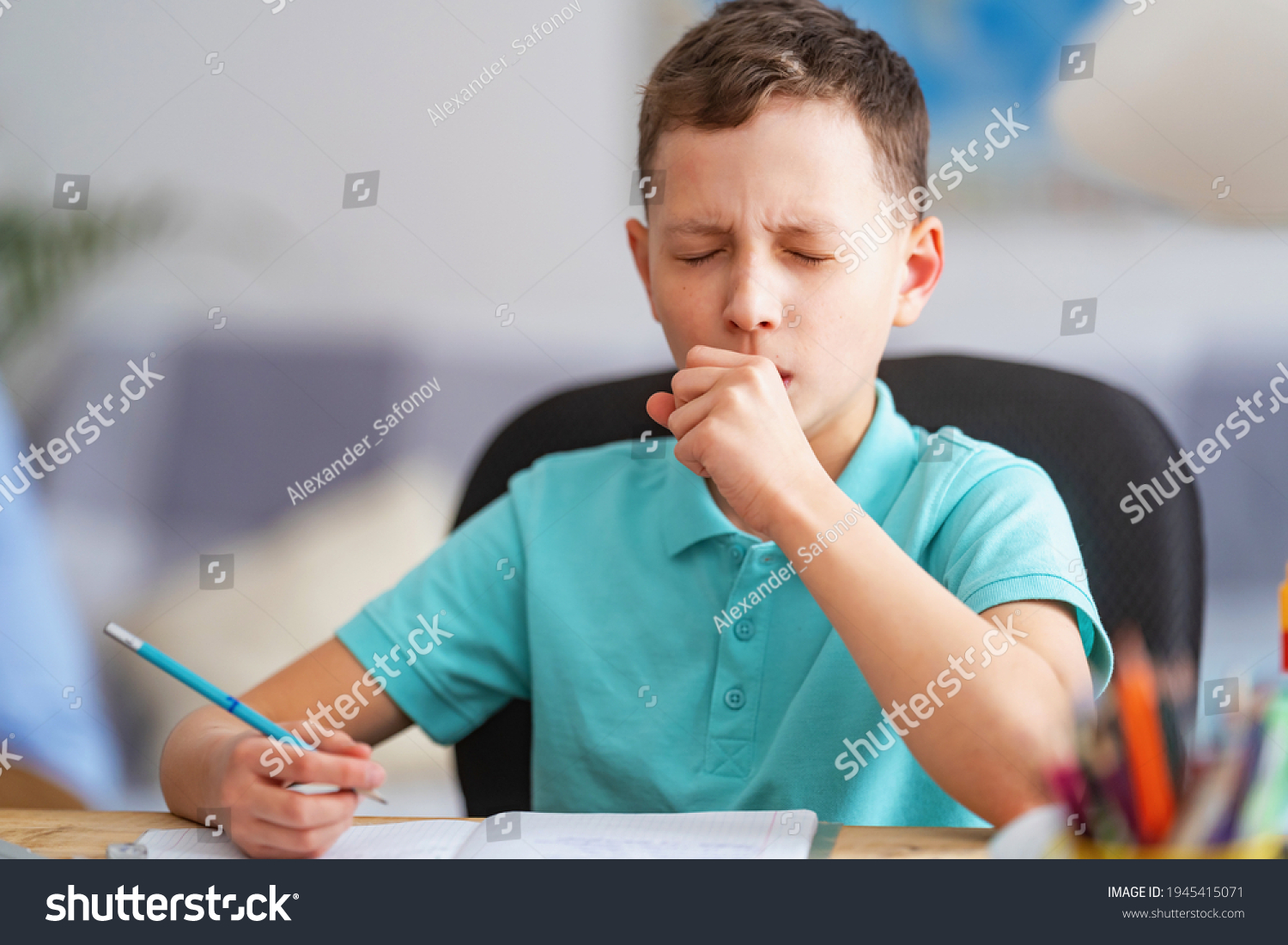 small child, schoolboy of 8 years old, is studying at a desk with laptop, at home. School distance education at home during quarantine concept. Coughing, sneezing, covering your mouth with your hand. #1945415071