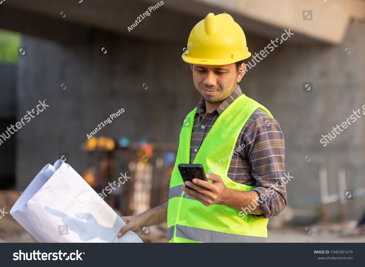 Asian construction workers using smartphone and holding blueprint at the construction site #1945581679