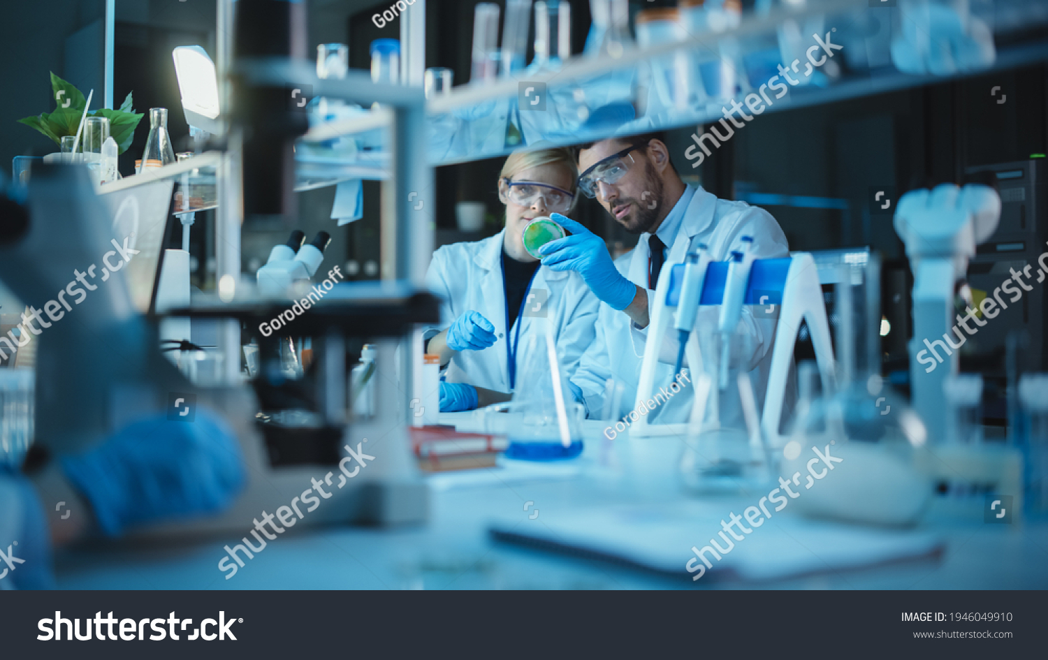 Female and Male Medical Research Scientists Have a Conversation While Conducting Experiments in Test Tubes with Liquid Samples with and in Beakers with Solid Speciments. Modern Science Laboratory. #1946049910