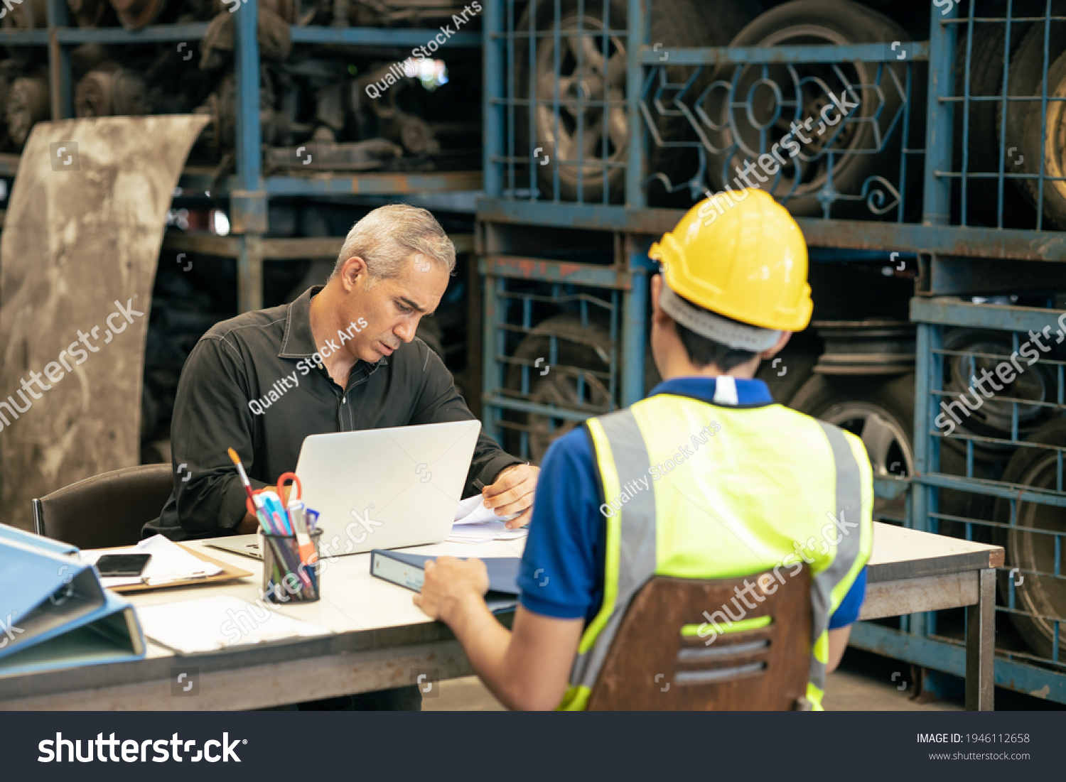 Factory manager looking at the paper with young engineer sitting front for call for blaming or consider and interview job apply or solving working problem report situation at factory work #1946112658