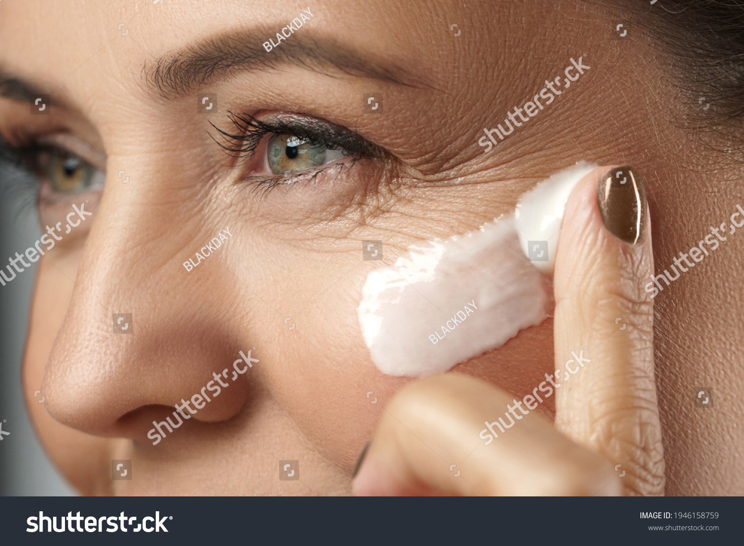 Beautiful middle aged woman applying anti-aging cream on her face on gray  #1946158759
