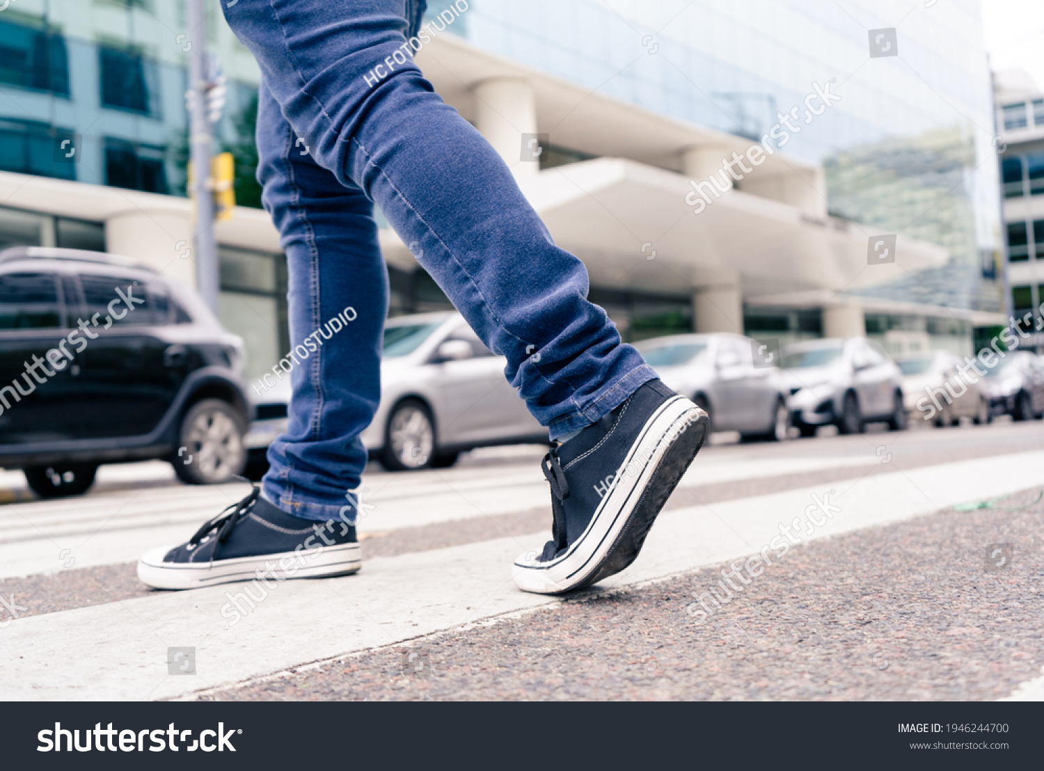 Close-up of the feet of a man in black sneakers crossing a street on the zebra or pedestrian path. #1946244700