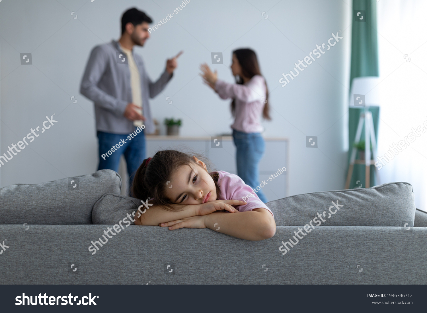 Family conflicts. Sad arab girl sitting alone, feeling lonely and depressed while her parents arguing on the background, selective focus. Family crisis and relationship problems #1946346712