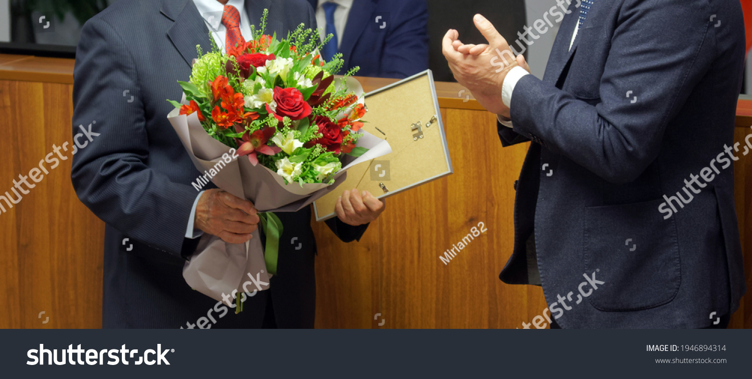 Men in business suits - officials, businessmen, teachers or lawyers - participants in the awards ceremony. Presentation of a certificate of honor and a bouquet of flowers. No face #1946894314