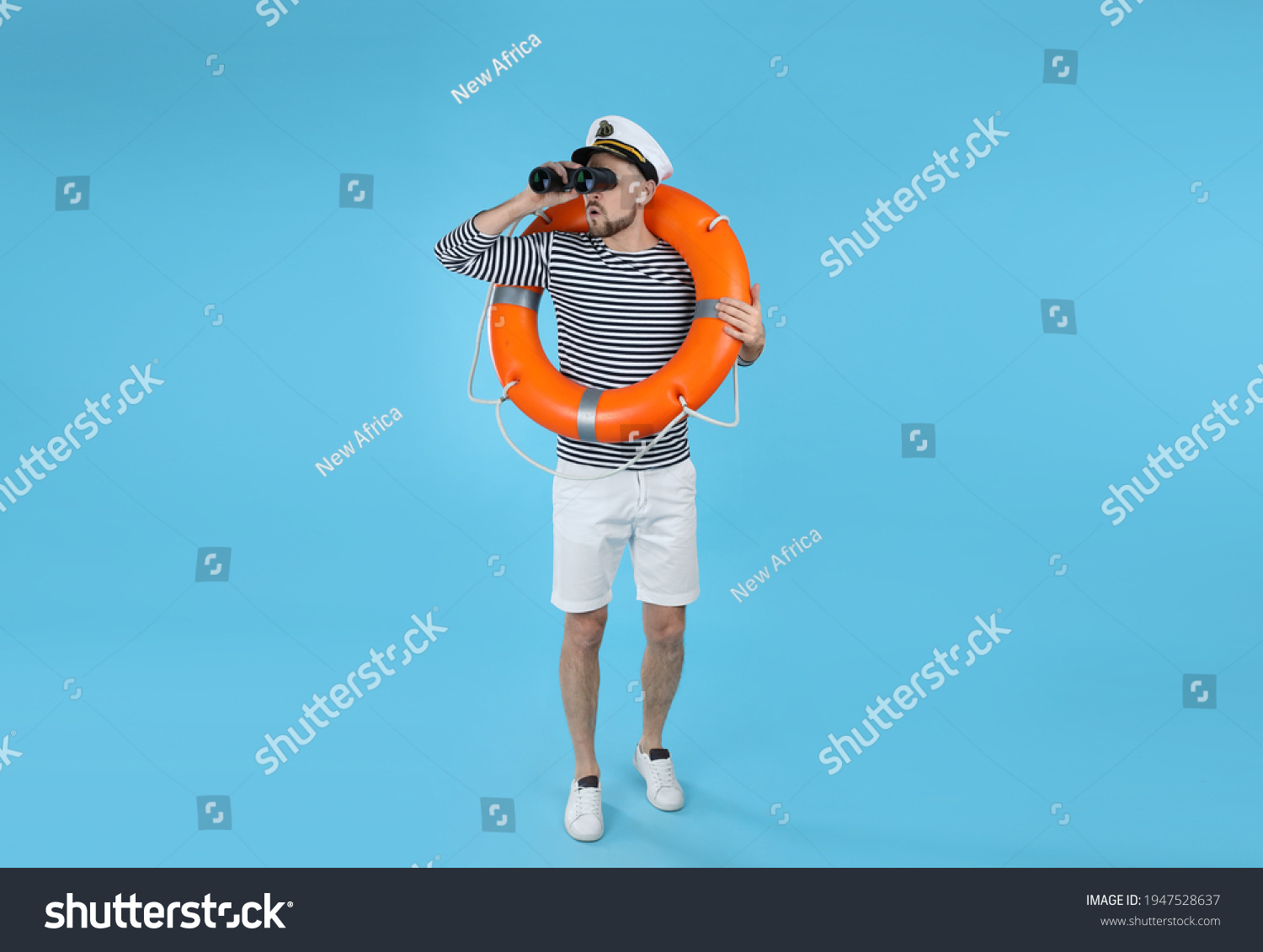 Sailor with orange ring buoy looking through binoculars on light blue background #1947528637