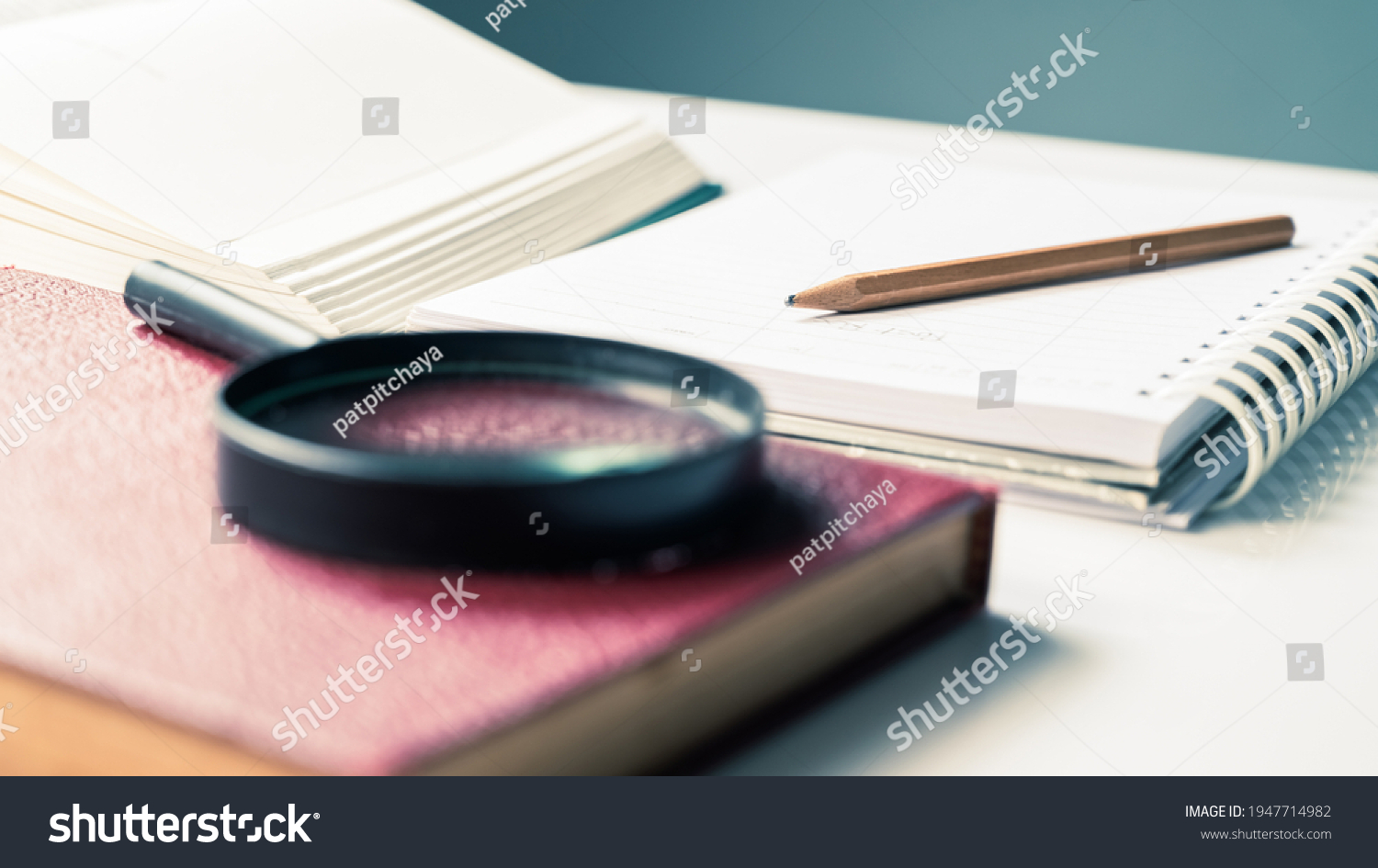 Closeup pencil on notebook with part of opened book and magnifying glass, reading for writing, summarize the content #1947714982