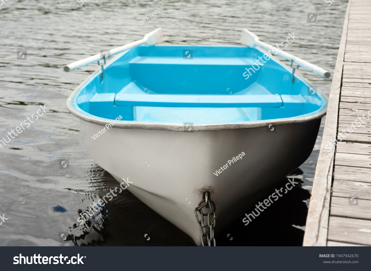 A blue and white boat with oars stands on the water at a wooden pier #1947942670