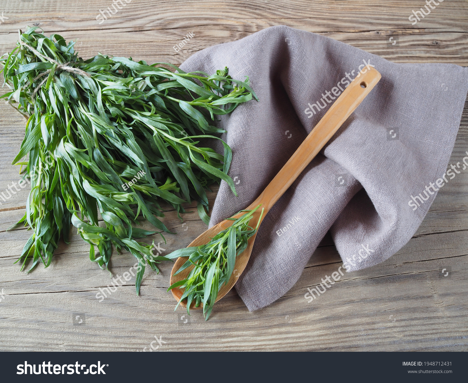 Fresh herb tarragon with a wooden spoon and napkin on a wooden table, flat layout. Aromatic medicinal herb artemisia dracunculus for the preparation of beverages and use in cooking #1948712431